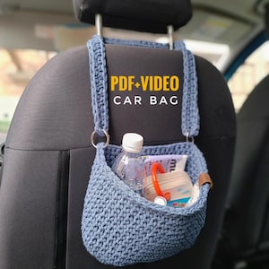 K&ouml;nnte beinhalten: Eine blaue geh&auml;kelte Autotasche, die an der Kopfst&uuml;tze eines Autositzes h&auml;ngt. Die Tasche ist gef&uuml;llt mit Gegenst&auml;nden wie einer Wasserflasche, einem Buch und ein paar anderen Kleinigkeiten. Der Text "PDF+VIDEO CAR BAG" ist in Gelb auf die Tasche gedruckt.