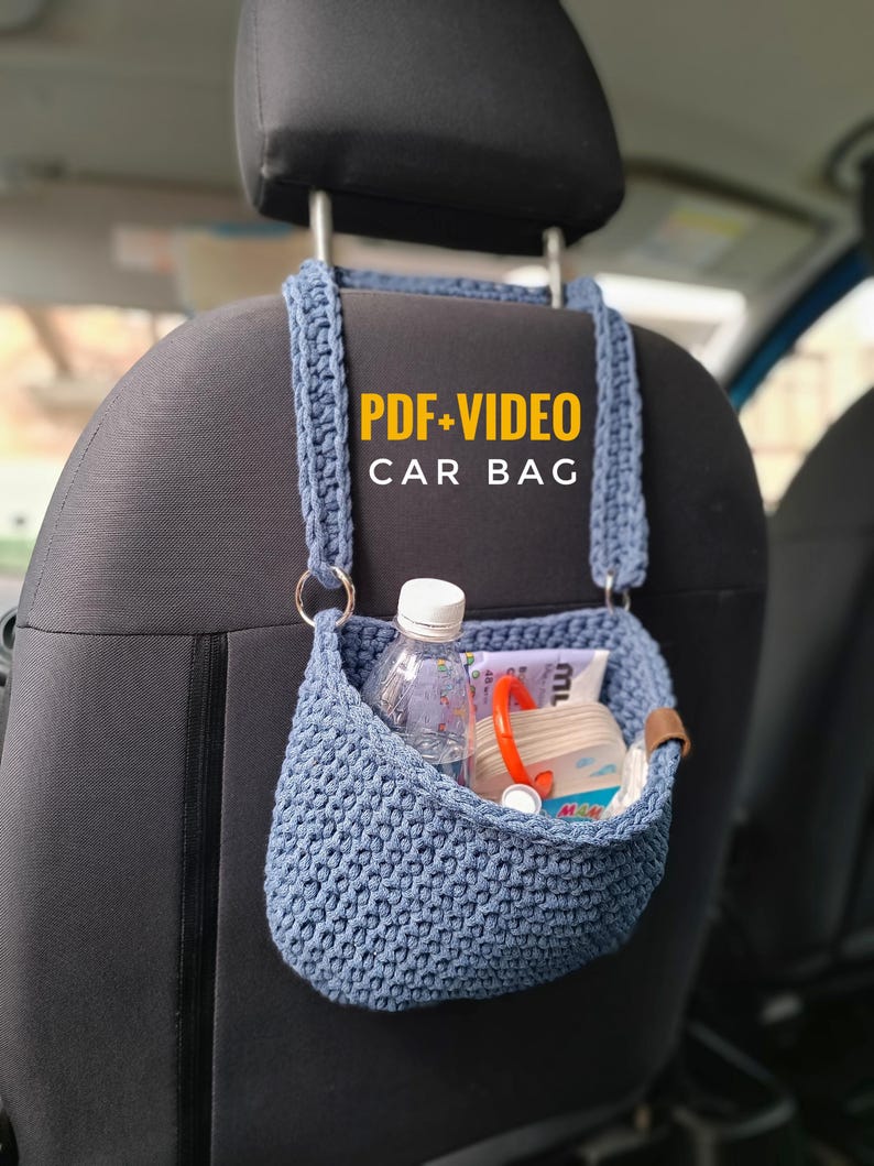 K&ouml;nnte beinhalten: Eine blaue geh&auml;kelte Autotasche, die an der Kopfst&uuml;tze eines Autositzes h&auml;ngt. Die Tasche ist gef&uuml;llt mit Gegenst&auml;nden wie einer Wasserflasche, einem Buch und ein paar anderen Kleinigkeiten. Der Text "PDF+VIDEO CAR BAG" ist in Gelb auf die Tasche gedruckt.