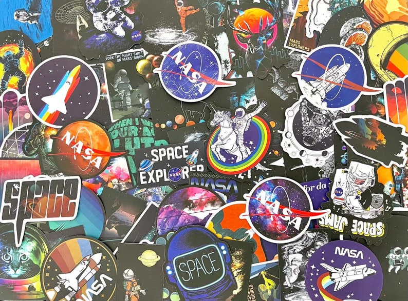 May include: A selection of space-themed stickers with diverse designs. The stickers depict rockets, planets, astronauts, and the NASA logo. Some stickers have text such as "SPACE EXPLORED" and "SPACE JAMS". The colour scheme includes blues, oranges, and purples.