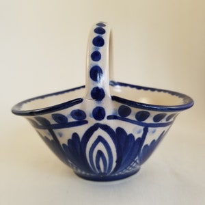 May include: A small white ceramic bowl with a blue and white floral design. The bowl has a handle and is perfect for serving snacks or holding small items.
