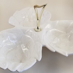 May include: White ceramic serving dish with three sections and a gold handle. The dish is shaped like a flower with a raised design.