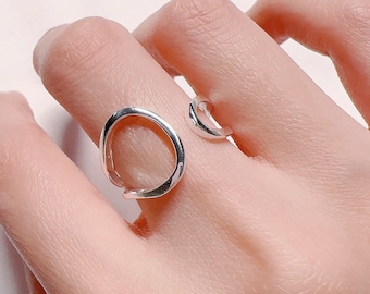Pode incluir: Um anel de prata com um design único de círculo aberto. O anel é feito de um metal liso e polido e tem uma estética moderna e minimalista.