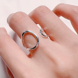 Op de afbeelding: Een zilveren ring met een uniek open cirkelontwerp. De ring is gemaakt van glad, gepolijst metaal en heeft een moderne, minimalistische esthetiek.