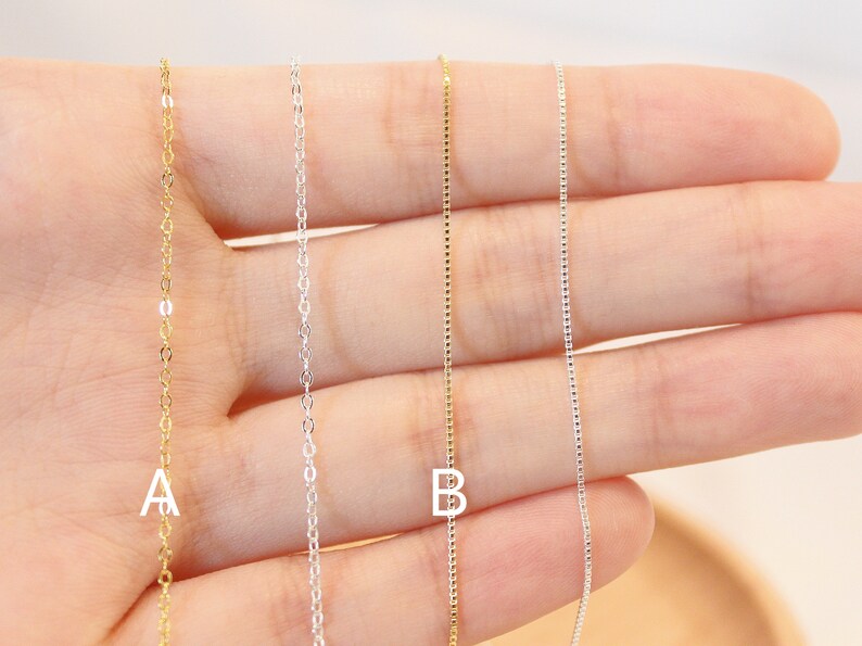 May include: Four delicate chains with letter charms, two gold and two silver. The chains are displayed on a hand, with the letter 'A' on the leftmost chain and the letter 'B' on the rightmost chain.