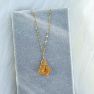 May include: A gold chain necklace with a raw, yellow-orange citrine pendant. The pendant is a natural, irregular shape.