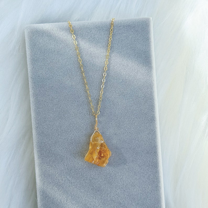 May include: A gold chain necklace with a raw, yellow-orange citrine pendant. The pendant is a natural, irregular shape.