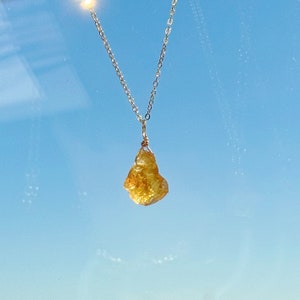 May include: A silver chain necklace with a raw, yellow citrine pendant.