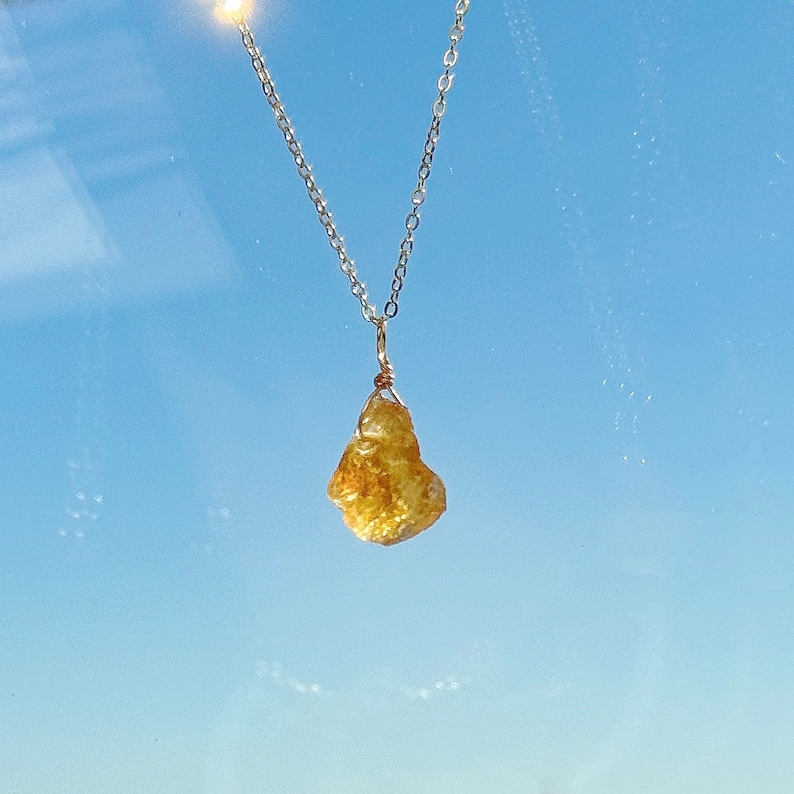 May include: A silver chain necklace with a raw, yellow citrine pendant.