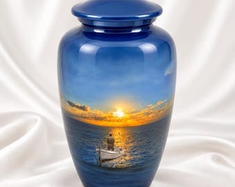 May include: A cylindrical cremation urn with a glossy deep blue finish. The exterior features a printed scene of a person in a small white boat on the ocean at sunset, with a bright yellow sun on the horizon and clouds in the sky.