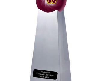 Puede incluir: Un trofeo plateado en forma de pirámide con una esfera burdeos en la parte superior que presenta un logotipo W en amarillo y burdeos. Una placa rectangular negra en el frente muestra el texto: Ron Johnson, Always in my Heart, 1940-1990.