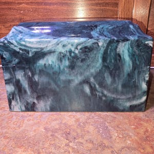 May include: A rectangular box with a marbled design in shades of teal, blue, and white. The box has a glossy finish and a slightly sloped top. The overall aesthetic is reminiscent of ocean waves.