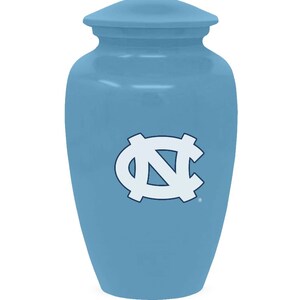 K&ouml;nnte beinhalten: Eine hellblaue Keramikurne mit einem wei&szlig;en und blauen Logo der North Carolina Tar Heels.