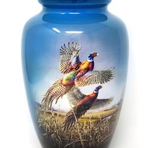 May include: Blue ceramic urn with a matching lid. The urn features a detailed painting of three pheasants in flight over a field. The birds have colorful plumage, and the background depicts a landscape.