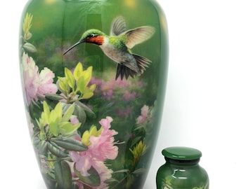 May include: Green ceramic urn and keepsake urn with a hummingbird and floral design. The urns feature a glossy finish and a detailed painting of a hummingbird in flight, surrounded by pink and yellow flowers.