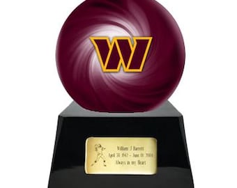 Puede incluir: Una esfera arremolinada de color burdeos y blanco con un logotipo W amarillo y burdeos, montada sobre una base trapezoidal negra con una placa rectangular dorada grabada con un jugador de fútbol americano y el texto William J Barrett April 30 1942 June 01 2004 Always in my Heart.