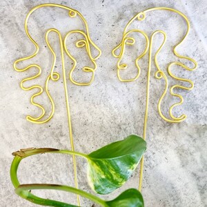 May include: Two gold wire sculptures of abstract faces facing each other. The sculptures are made of thin wire and have a simple, modern design.