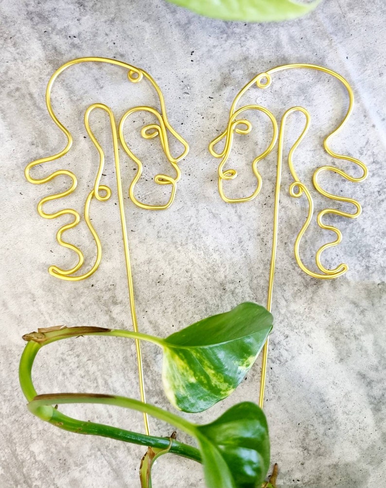 May include: Two gold wire sculptures of abstract faces facing each other. The sculptures are made of thin wire and have a simple, modern design.