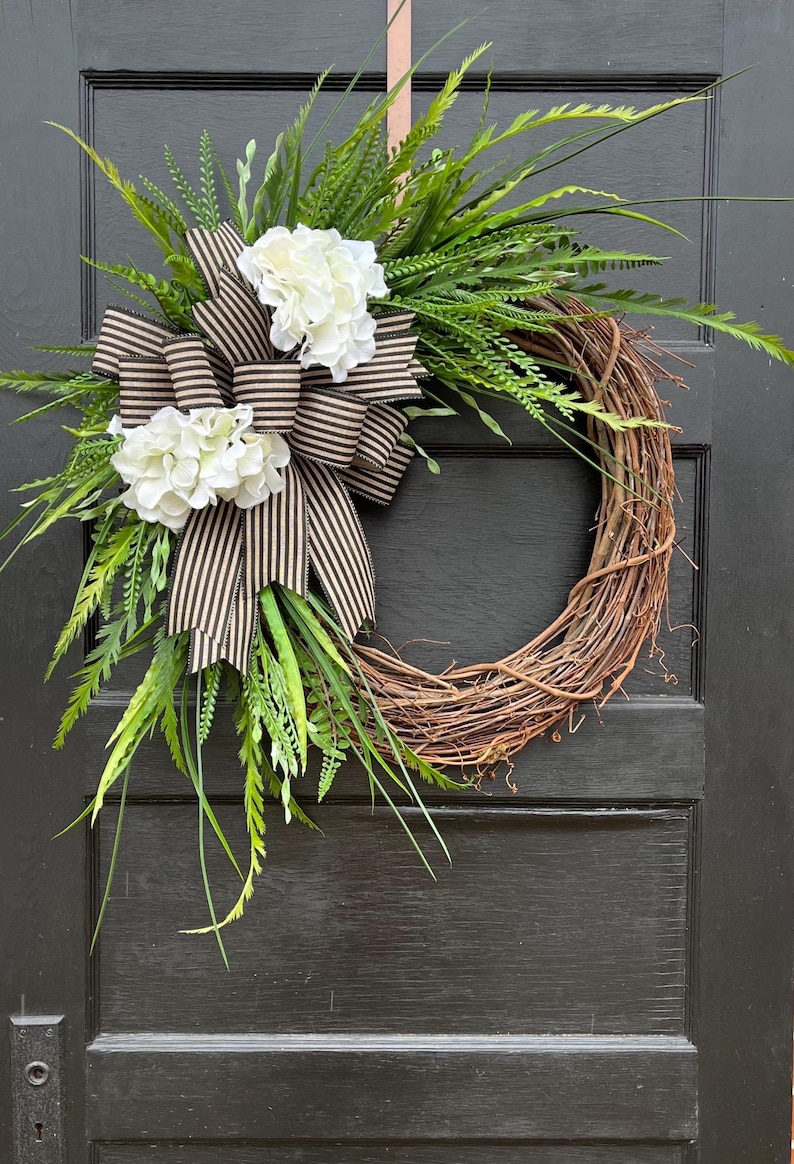 large outdoor greenery wreath with white hydrangea flowers and large striped burlap and black striped bow