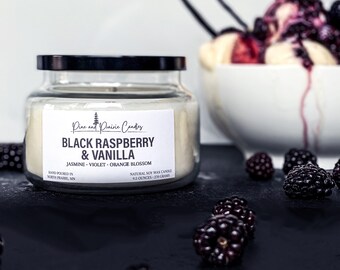 May include: A clear glass jar candle with a black lid. The candle is labeled "Pine and Prairie Candles" and "Black Raspberry & Vanilla". The label also lists the scent notes as "Jasmine, Violet, Orange Blossom". The candle is a natural soy wax candle and is 9.5 ounces or 270 grams.