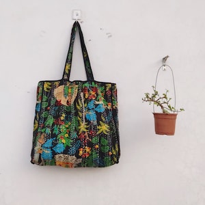 Könnte beinhalten: Eine schwarze Tragetasche mit einem Blumendruck mit bunten Blumen, Vögeln und anderen Designs. Die Tasche hängt an einer weißen Wand.