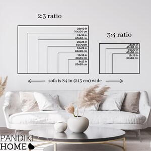 May include: A white sofa with two throw pillows sits in front of a white wall. A coffee table with a black top and gold legs sits in front of the sofa. A vase with dried flowers sits on the table. The wall behind the sofa has a diagram showing different sizes of artwork in inches and centimeters. The diagram is labeled "2:3 ratio" and "3:4 ratio". The text "sofa is 84 in (213 cm) wide" is written below the diagram.