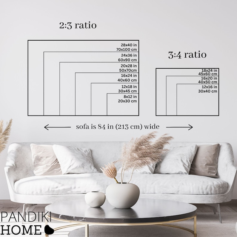 May include: A white sofa with two throw pillows sits in front of a white wall. A coffee table with a black top and gold legs sits in front of the sofa. A vase with dried flowers sits on the table. The wall behind the sofa has a diagram showing different sizes of artwork in inches and centimeters. The diagram is labeled "2:3 ratio" and "3:4 ratio". The text "sofa is 84 in (213 cm) wide" is written below the diagram.