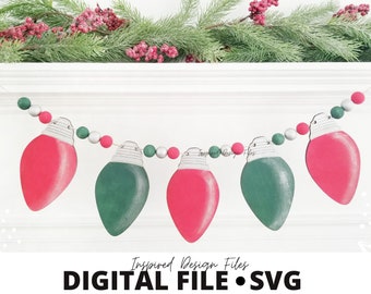 Può includere: Una ghirlanda natalizia con forme di lampadine rosse e verdi infilate con perline bianche e argentate. La ghirlanda è appesa a un camino bianco. Il testo "Inspired Design Files DIGITAL FILE. SVG" è in basso nell'immagine.