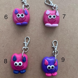 K&ouml;nnte beinhalten: Vier handgefertigte Schl&uuml;sselanh&auml;nger mit skurrilen Monstermotiven. Jeder Schl&uuml;sselanh&auml;nger hat einen silbernen Verschluss und eine farbenfrohe Monsterfigur. Die Monster sind rosa, lila und blau, mit Kulleraugen und l&auml;chelnden Gesichtern. Die Schl&uuml;sselanh&auml;nger sind etwa 5 cm hoch.