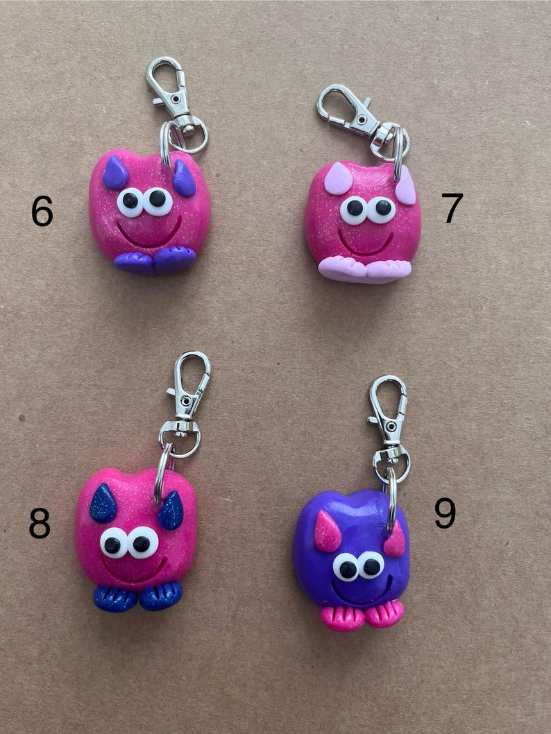 K&ouml;nnte beinhalten: Vier handgefertigte Schl&uuml;sselanh&auml;nger mit skurrilen Monstermotiven. Jeder Schl&uuml;sselanh&auml;nger hat einen silbernen Verschluss und eine farbenfrohe Monsterfigur. Die Monster sind rosa, lila und blau, mit Kulleraugen und l&auml;chelnden Gesichtern. Die Schl&uuml;sselanh&auml;nger sind etwa 5 cm hoch.