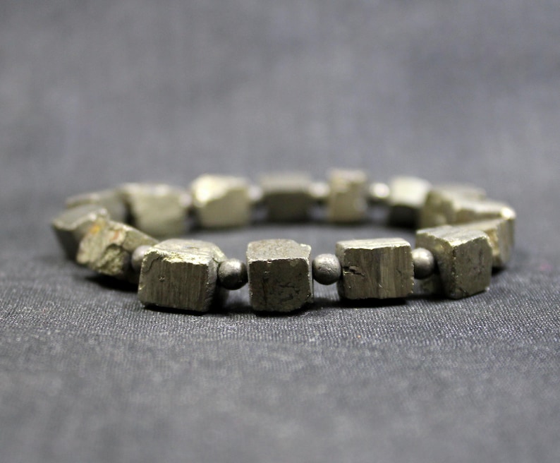 May include: A bracelet made of pyrite cubes, separated by small black beads. The bracelet is made of natural stone and has a rustic, earthy look.
