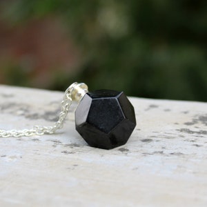 May include: A black geometric pendant necklace with a silver chain. The pendant is a dodecahedron, a 12-sided shape.