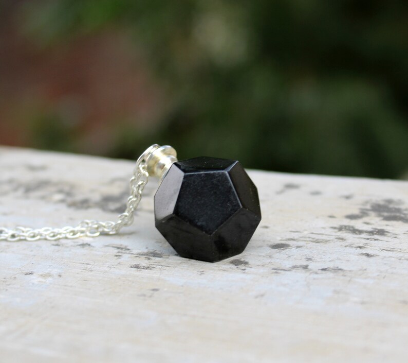 May include: A black geometric pendant necklace with a silver chain. The pendant is a dodecahedron, a 12-sided shape.