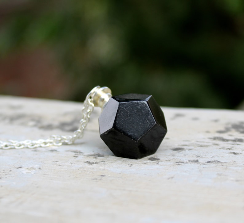 May include: A black geometric pendant necklace with a silver chain. The pendant is a 3D geometric shape with many facets.