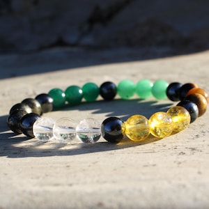 May include: A beaded bracelet featuring a variety of colorful gemstones. The bracelet includes clear, green, yellow, black, and brown beads. The beads are strung together to form a circular shape.
