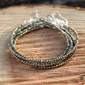 May include: Several strands of beaded bracelets in a circular arrangement. The beads are metallic grey. The bracelets are displayed on a wooden surface. The bracelets are a stylish accessory.