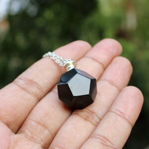 May include: A black geometric pendant necklace with a silver chain. The pendant is a dodecahedron, a 12-sided shape.