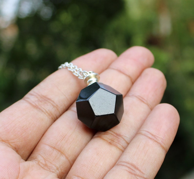 May include: A black geometric pendant necklace with a silver chain. The pendant is a dodecahedron, a 12-sided shape.