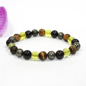 Puede incluir: Una pulsera de cuentas con una variedad de piedras preciosas en tonos marrón, amarillo, negro y gris. La pulsera está ensartada, mostrando los colores y texturas naturales de las piedras. La pulsera es una joya.