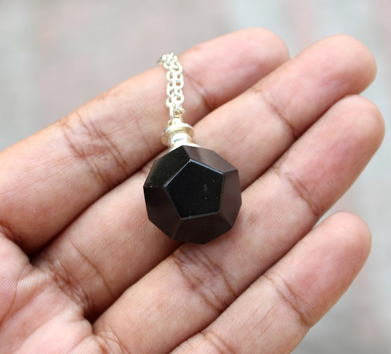 May include: A black gemstone pendant with a geometric shape, hanging from a silver chain.