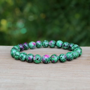 Puede incluir: Un brazalete de piedras preciosas verdes y rosas con cuentas redondas. El brazalete está hecho de piedras naturales y es una opción popular para quienes disfrutan de usar joyas con un aspecto natural.