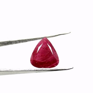 May include: A deep red pear-shaped gemstone held by tweezers against a white background.