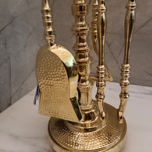 May include: A gold metal fireplace tool set with a hammered finish. The set includes a shovel, poker, and tongs. The tools are mounted on a stand with a round base.