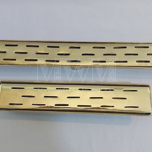 May include: Two gold-colored metal drain covers with a rectangular shape and a slotted design. The larger drain cover is about 12 inches long and the smaller drain cover is about 6 inches long.