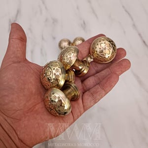 Puede incluir: Un juego de cinco pomos de puerta de latón con intrincados diseños florales. Los pomos son redondos y tienen un acabado pulido.