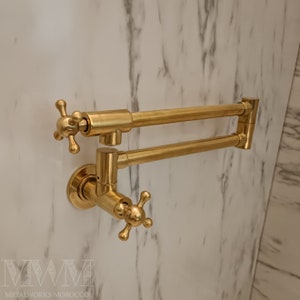 May include: A gold-toned kitchen tap with a swivel spout and two cross-shaped handles. The tap is mounted to a wall.
