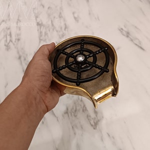 K&ouml;nnte beinhalten: Eine goldfarbene Metall-Seifenschale mit einem schwarzen, radartigen Seifenschwamm aus Kunststoff im Inneren. Die Schale hat einen Ausguss zum Abtropfen von Wasser.