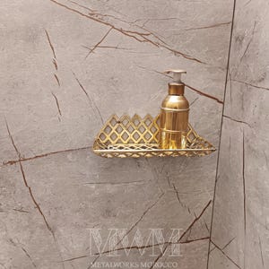 May include: Gold metal shelf with a decorative geometric design. A gold bottle with a pump dispenser is on the shelf.