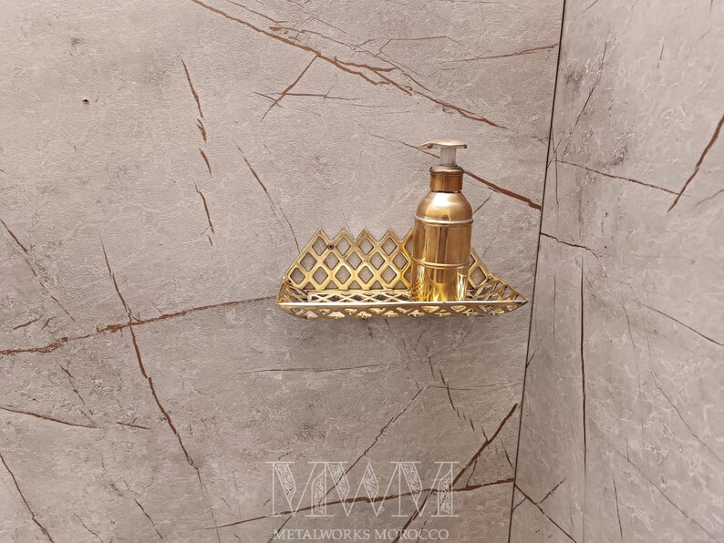 May include: Gold metal shelf with a decorative geometric design. A gold bottle with a pump dispenser is on the shelf.