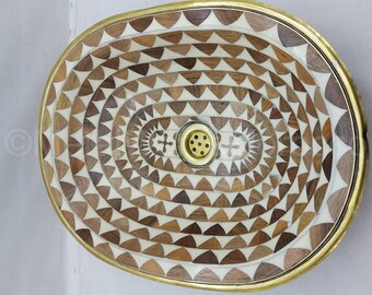 Op de afbeelding: Ovaalvormige wastafel gemaakt van hout en messing met een geometrisch patroon van driehoeken. De wastafel heeft een messing afvoer in het midden.
