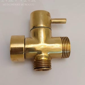 Puede incluir: Una v&aacute;lvula desviadora de ducha de lat&oacute;n de color dorado con tres salidas. La v&aacute;lvula tiene una conexi&oacute;n redonda y roscada en la parte inferior y dos conexiones roscadas en los lados. La v&aacute;lvula tiene una peque&ntilde;a palanca en la parte superior para cambiar entre las salidas.